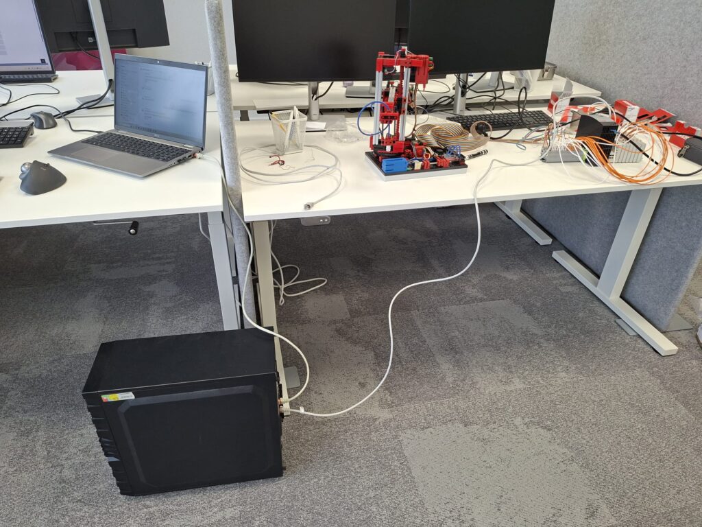 Fischertechnik automatiseringsmodel op een bureau bij Brisq, verbonden met een industriële PC en bekabelde I/O-hardware