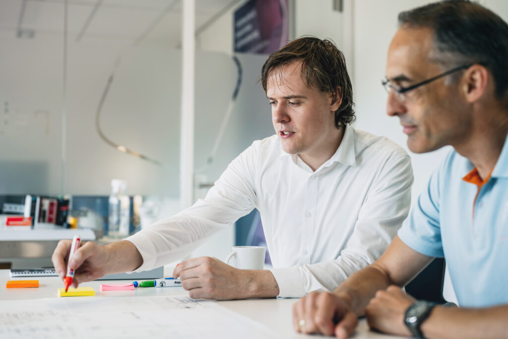Senior/lead engineer aan een tafel, ontwerptekeningen aan het uitleggen aan andere engineers.